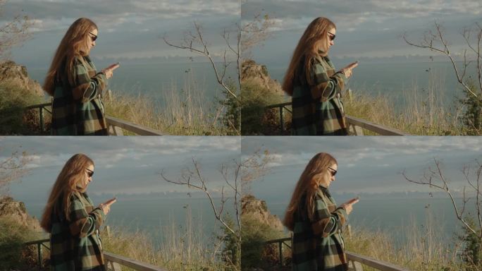 海风吹乱了站在海边悬崖边看手机的年轻女子的长发。