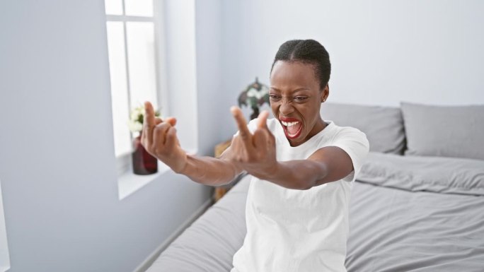 一名非裔美国女性在卧室里竖起中指示意“去你的”。表现出不好的态度和挑衅，她躺在床上表现出粗鲁的行为!