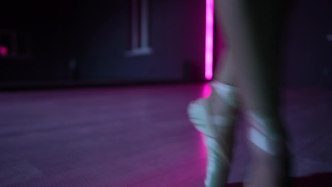 住相机。在霓虹灯照亮的黑暗舞蹈大厅里，芭蕾舞女演员优美动作的特写。
