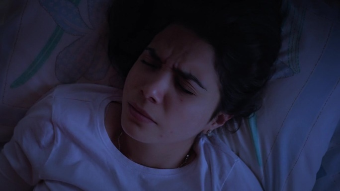 俯视图，一个西班牙裔受打扰的年轻女子晚上躺在床上做恶梦用闪光灯