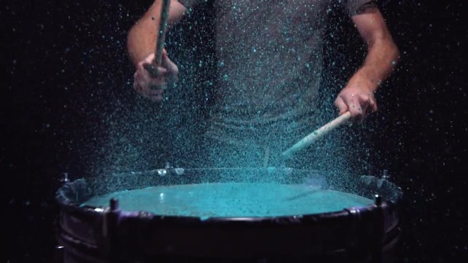 一个人在打鼓，鼓里装满了蓝色的颜料，当鼓槌以慢动作敲击时，颜料会飞溅出来。