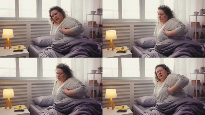 超重的女人抱着胸口，坐在床上痛苦不堪，心脏病发作