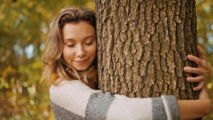 秋林中抱树微笑少女的特写