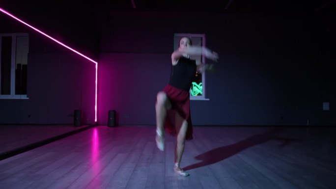 一位美丽的芭蕾舞女演员在黑暗的舞蹈大厅里用霓虹灯照亮的镜子跳舞。舞蹈女子的优美的芭蕾舞动作。