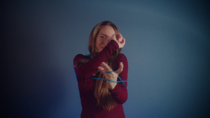 被绑起来的女孩的肖像在蓝色背景上解开酒红色毛衣的绳子