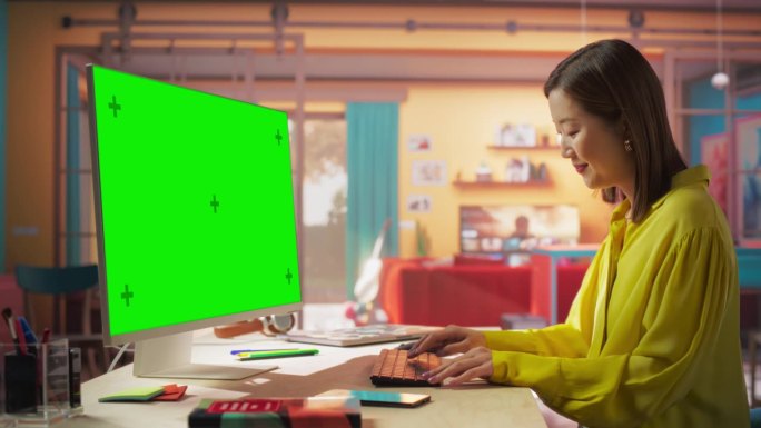 美丽的专业亚洲妇女工作在她的个人电脑与大绿屏模拟显示。创意女性作品在一个很酷的阁楼空间。学习与职业概