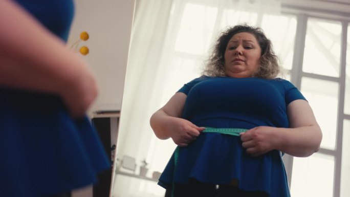 肥胖妇女测量腰围的下视图，不高兴大肚子，超重