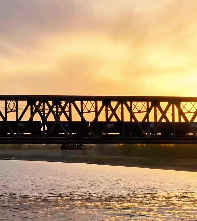 竖版列车通过彩霞映衬的河流桥梁