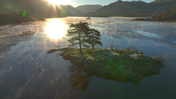 平静的湖面上的小岛，轻柔的薄雾在水面上盘旋，轨道上露出冉冉升起的太阳和被树木遮挡的反射。秋天。乌尔斯