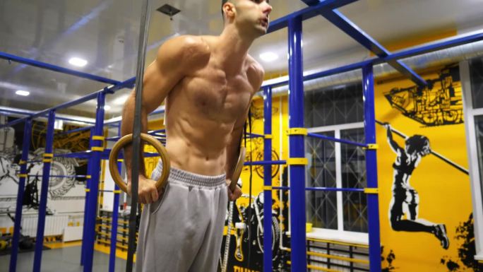 强壮的运动员在现代健身房的体操环上做俯卧撑。肌肉发达的赤膊运动员在健身俱乐部努力锻炼。年轻男子体操运