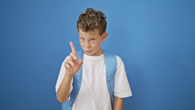 可爱的金发男学生指着自己微笑，用手指在孤立的蓝色背景上说“不”，散发出快乐的否定