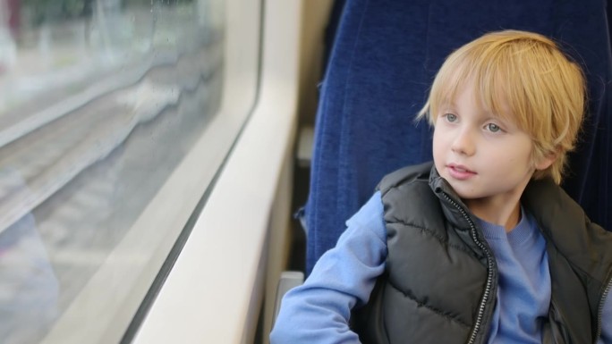 可爱的青春期前男孩在外面下雨的时候坐在地铁车厢或火车上。