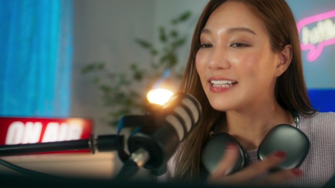 快乐的年轻亚洲女主播带着耳机在电脑上玩在线视频游戏，快乐的年轻女玩家享受着直播