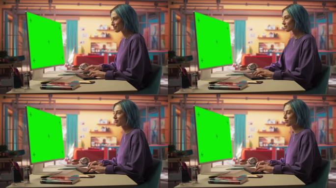 静态肖像美丽时尚的女人与蓝头发使用现代桌面电脑与绿屏模拟显示。创意女性设计师和程序员从时尚之家工作