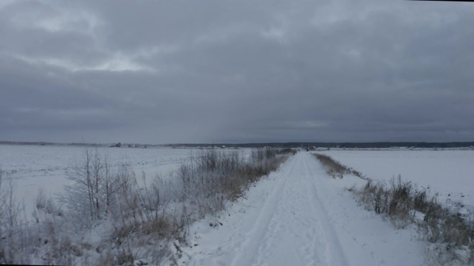无人机拍摄的乡村道路上积雪上的汽车轨迹，背景是阴暗的黄昏天空