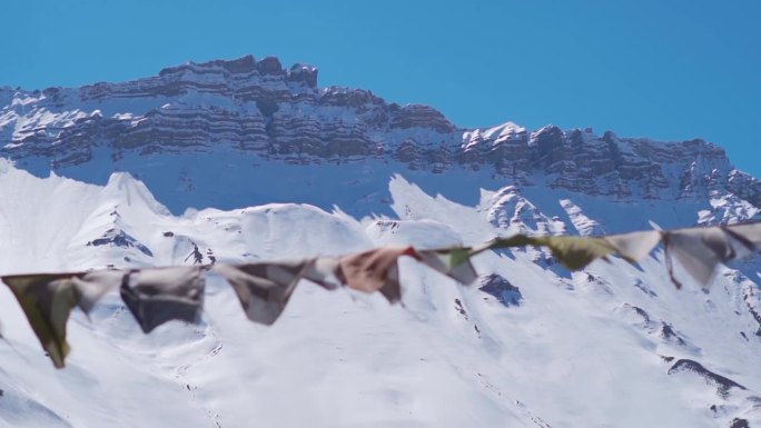 冬季，印度喜马偕尔邦斯皮提山谷的卡扎，白雪覆盖了喜马拉雅山峰，前面的祈祷旗在风中飘扬。喜马拉雅山的经