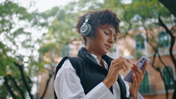 女孩耳机使用手机应用程序在户外听音乐。女人选歌。