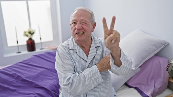 一位兴高采烈的老人坐在卧室里，穿着睡衣，对着胜利的眼睛和和平的手势微笑着庆祝胜利