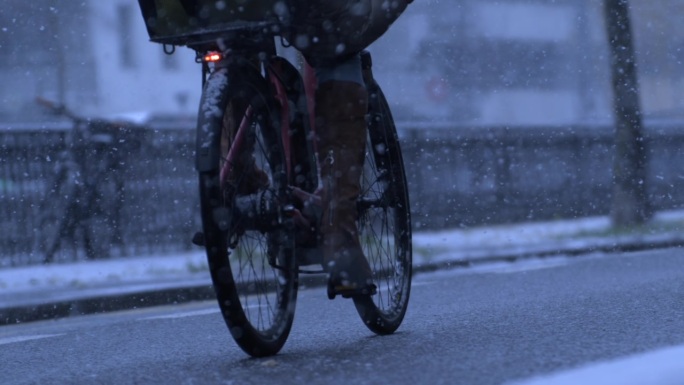 一个人在城市里的雪中骑自行车，以1000帧/秒的速度拍摄，冬天的城市环境