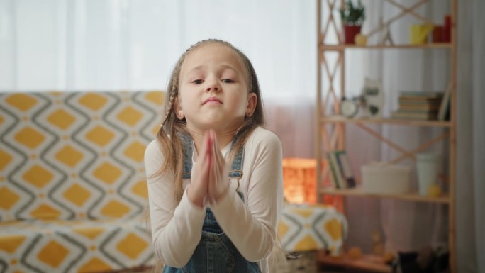 一个初中女生用手掌做祈祷的手势问道。一名初中女生用手掌做祈祷手势并握手。金发小孩站在明亮舒适的房间里