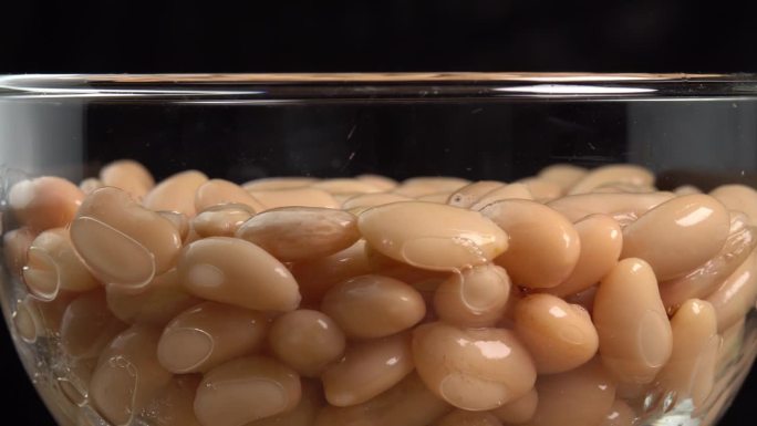 白芸豆罐头在玻璃碗里旋转。墨西哥菜的腌豆。有机蒸豆