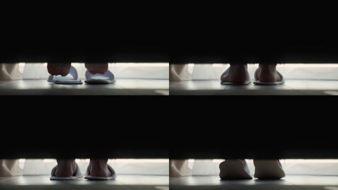 一个女人穿上白色拖鞋，从酒店房间的地板上爬起来。客人把脚穿上拖鞋，下床，离开特写镜头