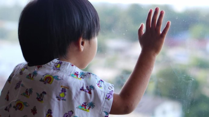 一个亚洲小孩望向窗外，希望到外面去玩。