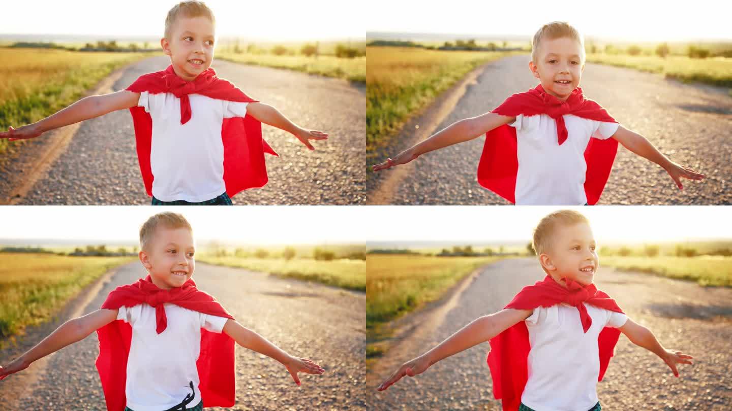 男孩扮演超级英雄。快乐的小男孩在玩超级英雄。日落时分，小孩穿着红斗篷跑过马路。在大自然中穿着红色斗篷