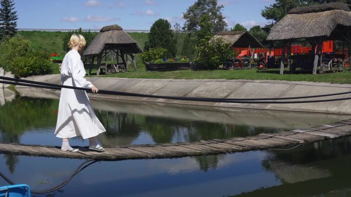 一个女孩走在池塘上的绳木桥上，保持着平衡。