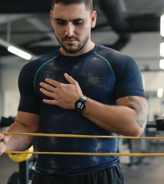 身穿运动服的肌肉男运动员在健身房用健身橡皮筋锻炼