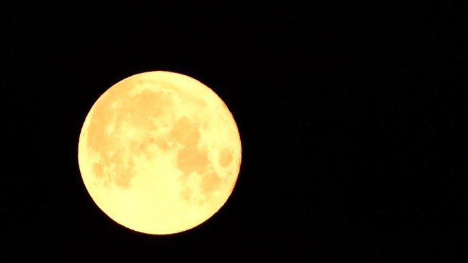 从地球上透过大气层看到的金色满月，映衬着繁星点点的夜空。一轮巨大的满月划过天空，月亮从左边的画面移向