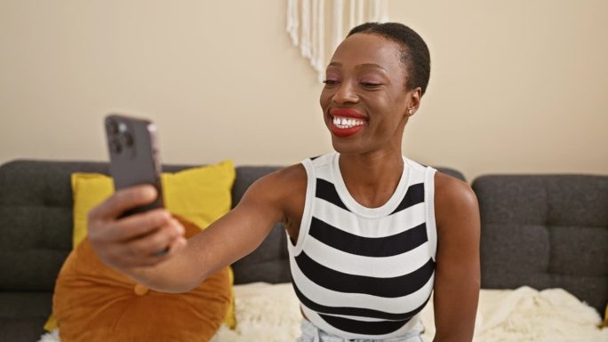一位快乐的非裔美国妇女坐在家里舒适的沙发上，脸上洋溢着灿烂的笑容，正在进行生动的视频通话。