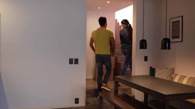 一对年轻夫妇搬着箱子，搬上新房的楼梯