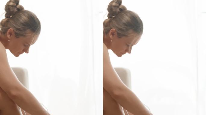 垂直视频。一个裹着毛巾的年轻女子坐在沙发上，在淋浴后使用照片脱毛器，代表了家庭护肤的概念。场景发生在