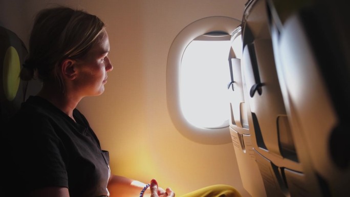 女乘客正在飞机上飞行。女孩坐在飞机上望着窗外去旅行度假旅行。旅行中的女性在飞机上享受飞行。旅行的女孩