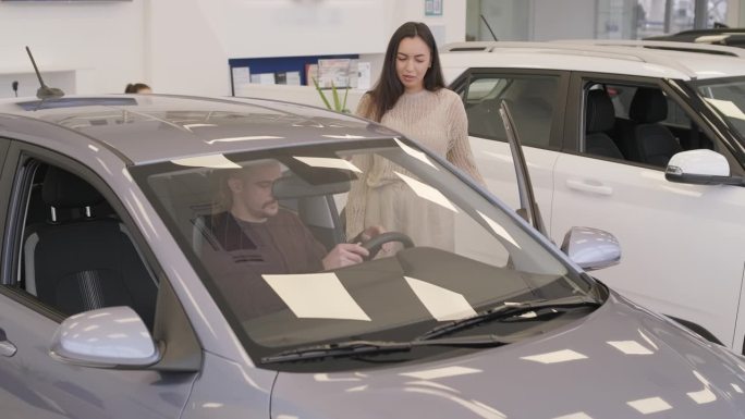 漂亮的年轻夫妇在汽车展示厅挑选新车。