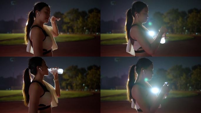 年轻的亚洲女性在跑道上跑了一晚后，停下来喝水，查看智能手表上的跑步数据