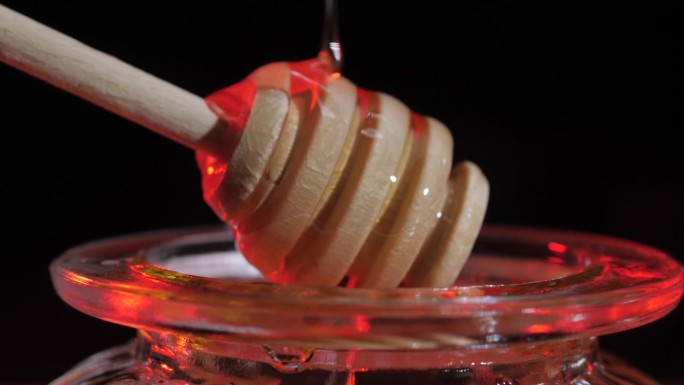 液体新鲜蜂蜜。蜂蜜滴着，从蜜罐里倒出来。木制蜂蜜勺。健康食品。