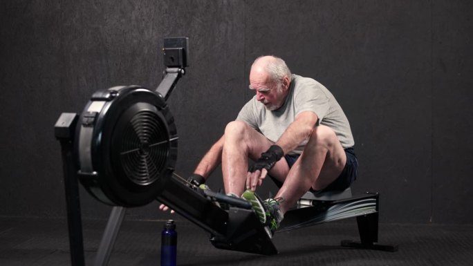 近距离观察五六十岁的老人在划船机上训练双手。健康老年男性健身或室内快速热身。积极的生活方式或健康的老