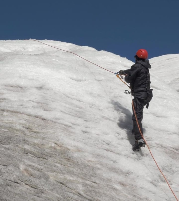 戴着冰爪和头盔的登山队员在山坡上使用固定绳上的上升器。垂直视频