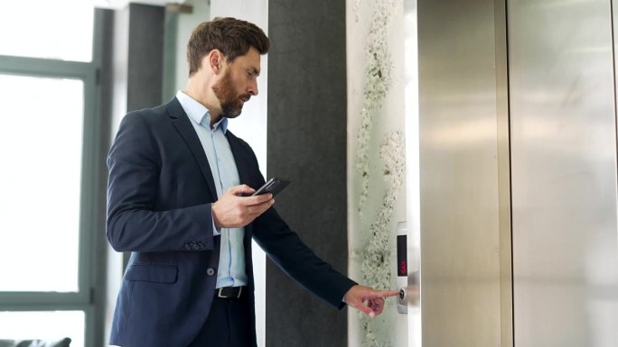 一个商人在现代写字楼里打电话给电梯，用智能手机浏览网页。
