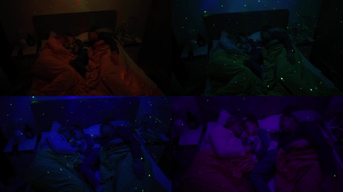 父母带着儿子睡在床上，床上有一盏白噪音RGB灯，灯上的星星投射在墙上