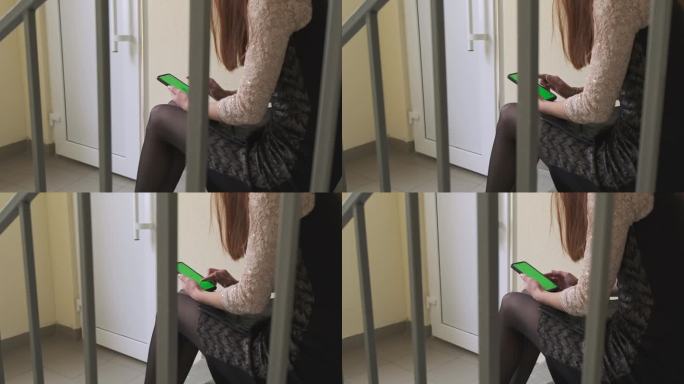 一位女士正坐在门前的水泥楼梯上。用智能手机求救。绿色的屏幕。这个女人不能回家，她忘了带钥匙，打电话给