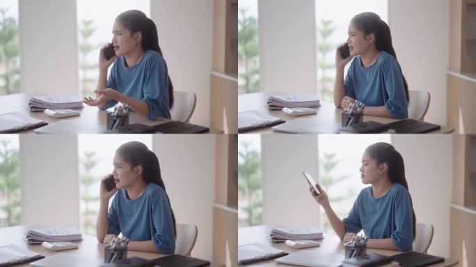 一个沮丧沮丧的亚洲女人，穿着休闲服，正在进行一场激烈而难以理解的电话交谈。她心情沉重地把电话放在餐桌