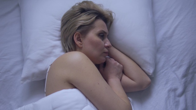 烦躁不安的女人躺在床上，试图入睡，患有失眠，昼夜节律问题，睡眠阶段障碍
