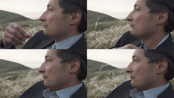 一个穿着西装的严肃的成年男子的特写侧面肖像，背景是野生的自然