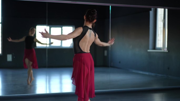 芭蕾舞演员在舞蹈大厅练习。一个美丽的女人注视着镜子里的自己，完善着她的动作。