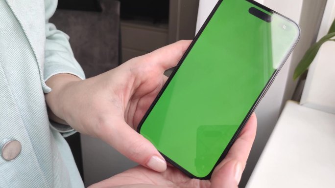 一个小女孩的手拿着一个绿色屏幕的智能手机，向镜头近距离展示