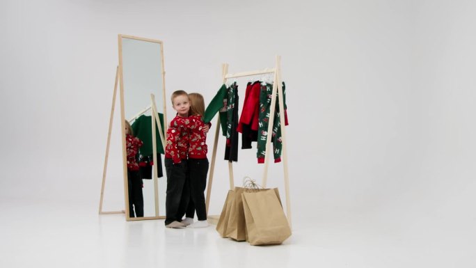 浅色背景下的孩子们在更衣室里，背景是挂着孩子衣服的衣架。圣诞夜的小时尚达人。