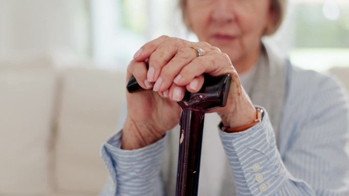 手杖，手和老年妇女在客厅的沙发上退休的房子。拐杖，沙发和残疾老人的特写，拐杖受伤和支持，帮助和骨质疏